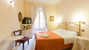 A bedroom with a bed, a chair, a small table, a television, and a window with curtains. - Marta Guest House (Rome)