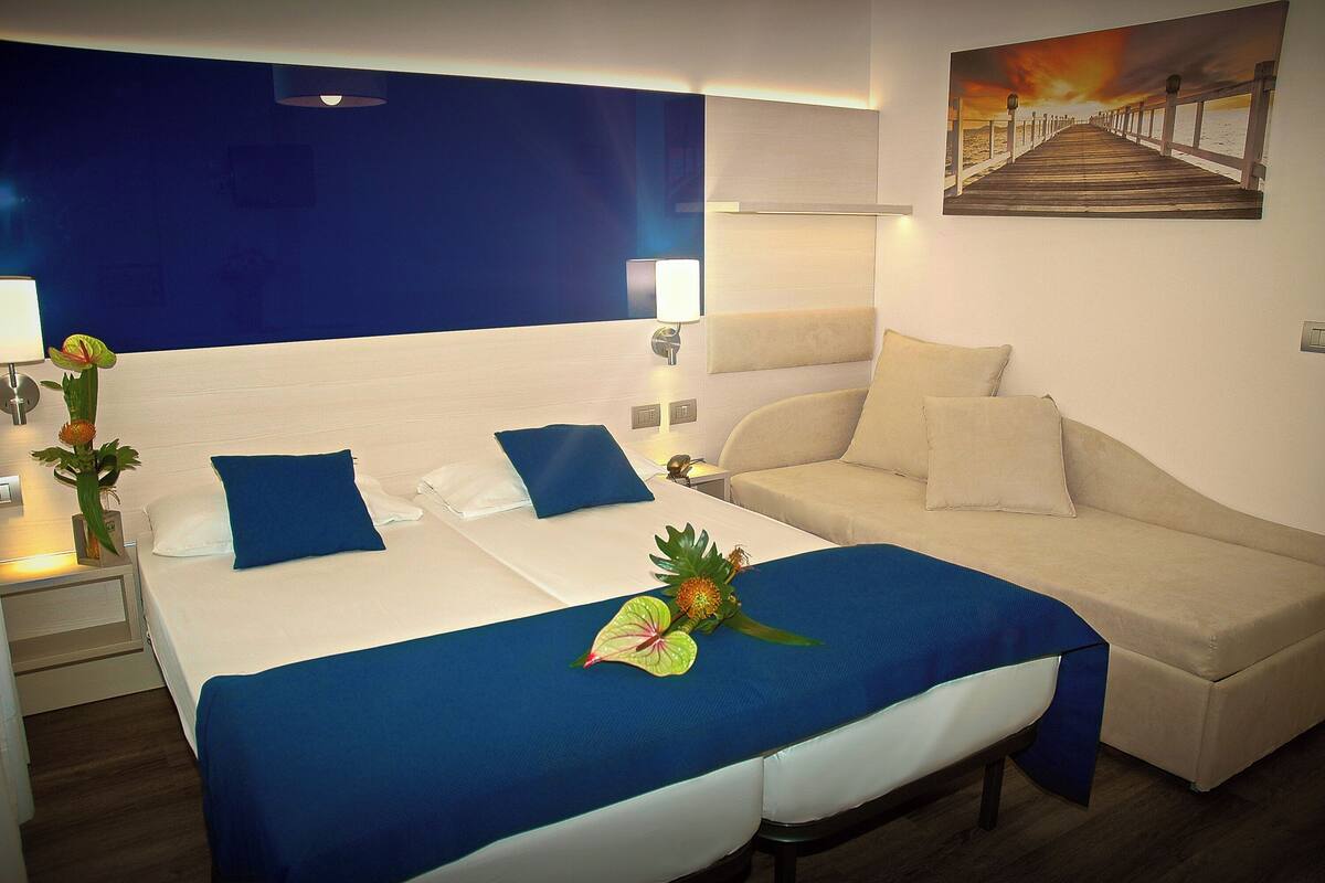 Une chambre d’hôtel avec un lit, un canapé, une table de chevet, une lampe et un tableau au mur.