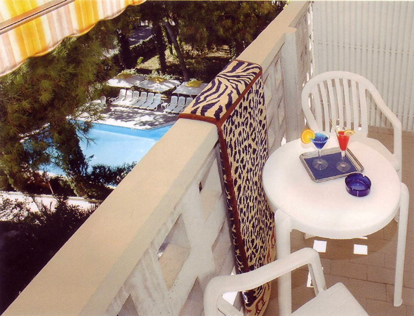 Ein Balkon mit Blick auf einen Pool, weiße Stühle, ein Kissen mit ZEBRA-Muster sowie ein Tisch mit Getränken und einer Serviertablett.