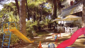 Un terrain de jeux avec des toboggans et une balançoire, entouré d’arbres et agrémenté de mobilier d’extérieur.