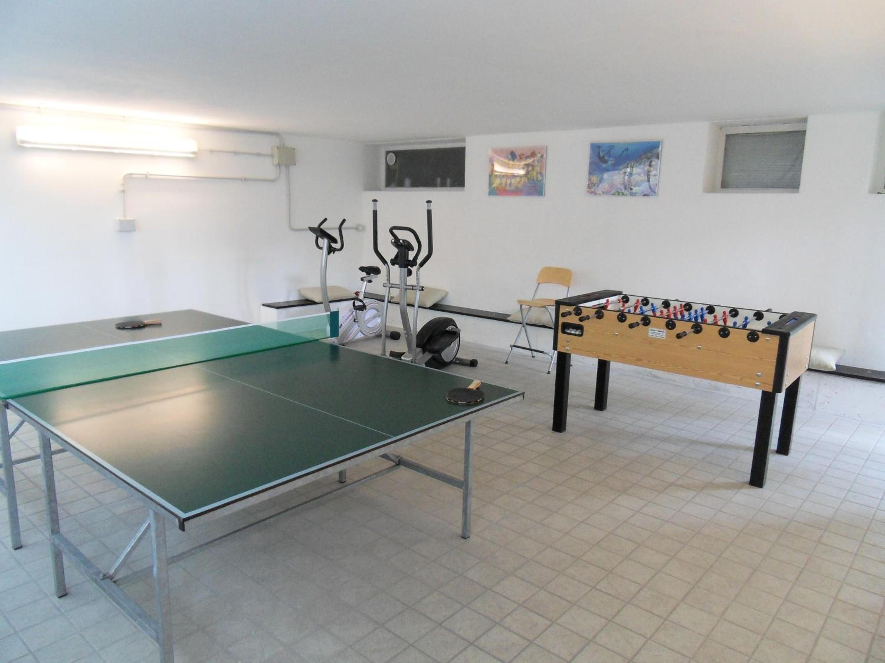Una habitació amb taula de ping-pong, taula de futbolí, equip d'exercici i obres d'art a les parets.