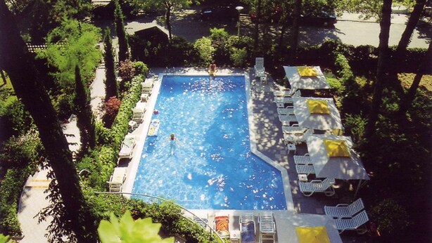 Une piscine rectangulaire entourée de chaises longues et de parasols, avec des arbres et un sentier en arrière-plan.