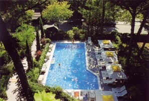Une piscine rectangulaire entourée de chaises longues et de parasols, avec des arbres et un sentier en arrière-plan.