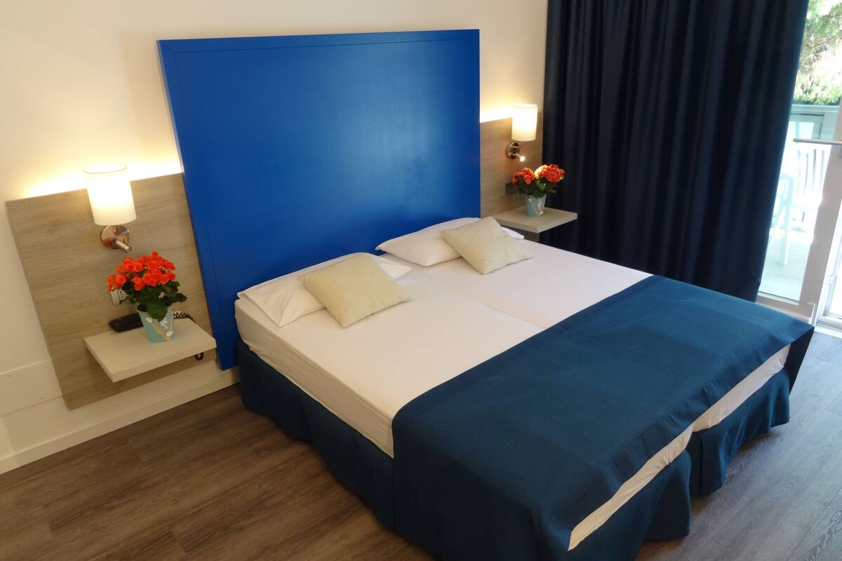Une chambre d’hôtel avec un grand lit, une table de chevet avec une lampe et une fenêtre avec des rideaux.