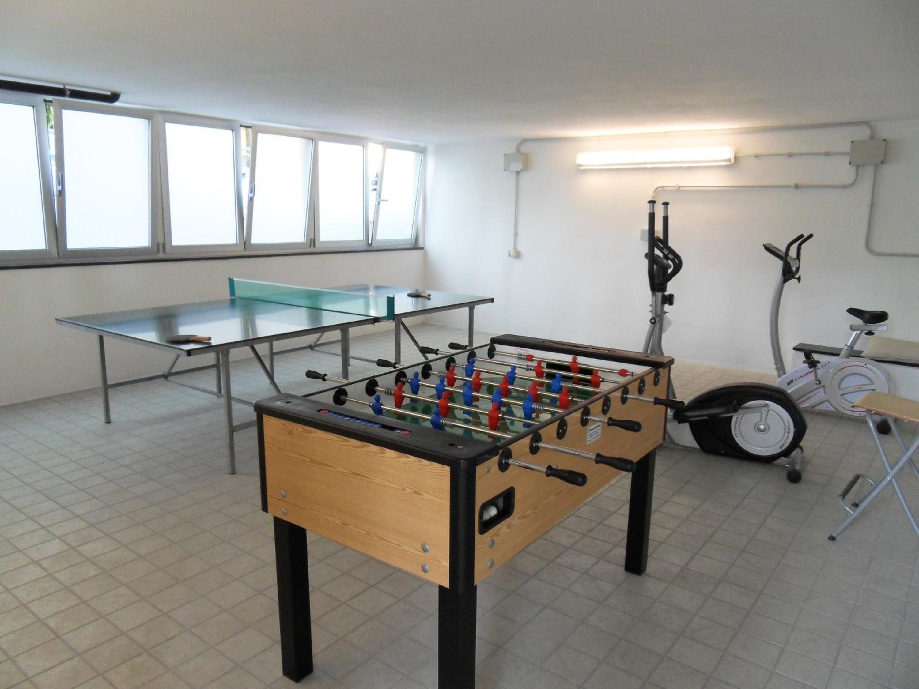 Una habitación con mesa de fútbol de mesa, mesa de ping pong y una bicicleta estática.