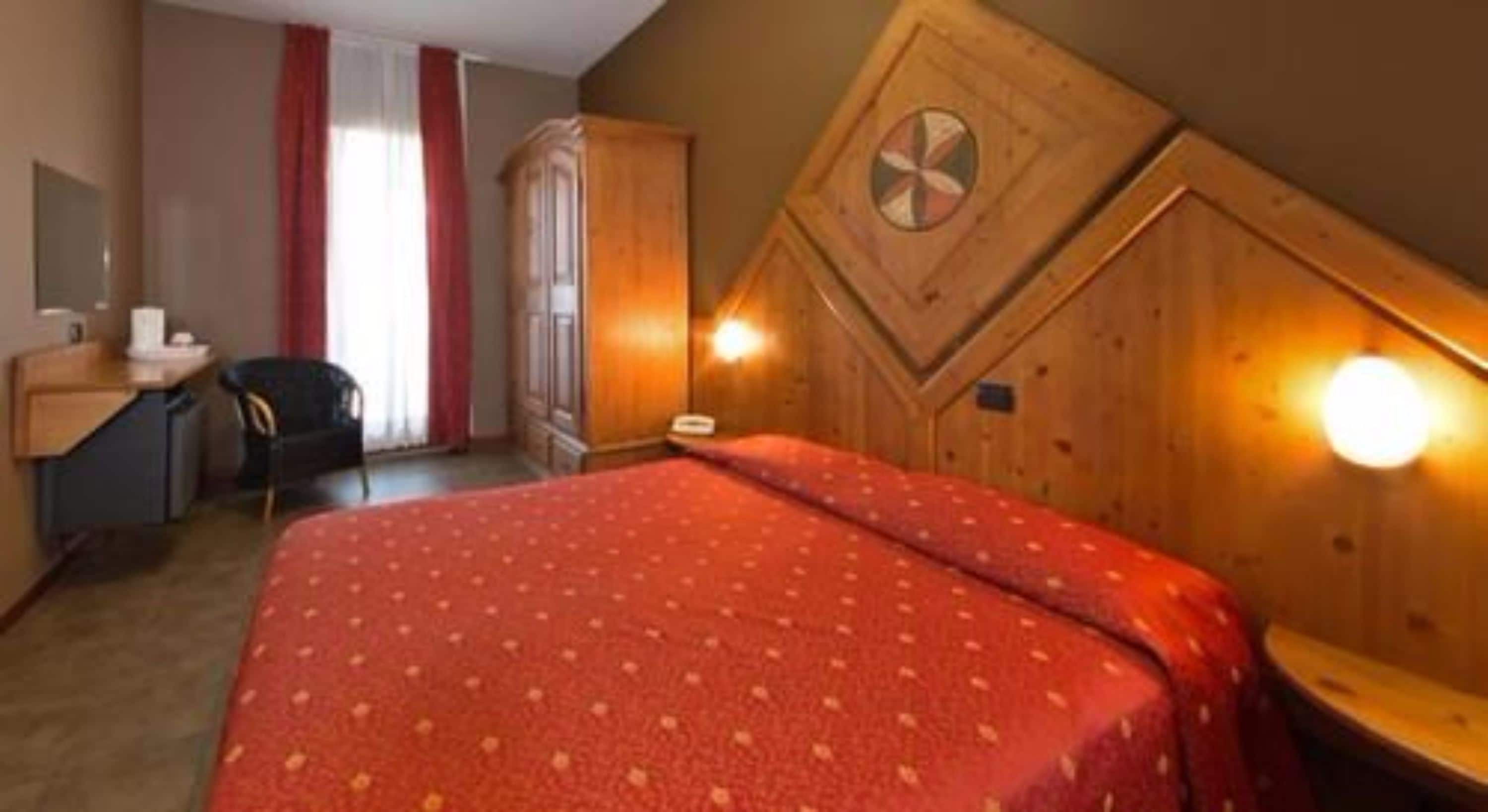 Et hotelværelse med seng, skrivebord, stol og skab.