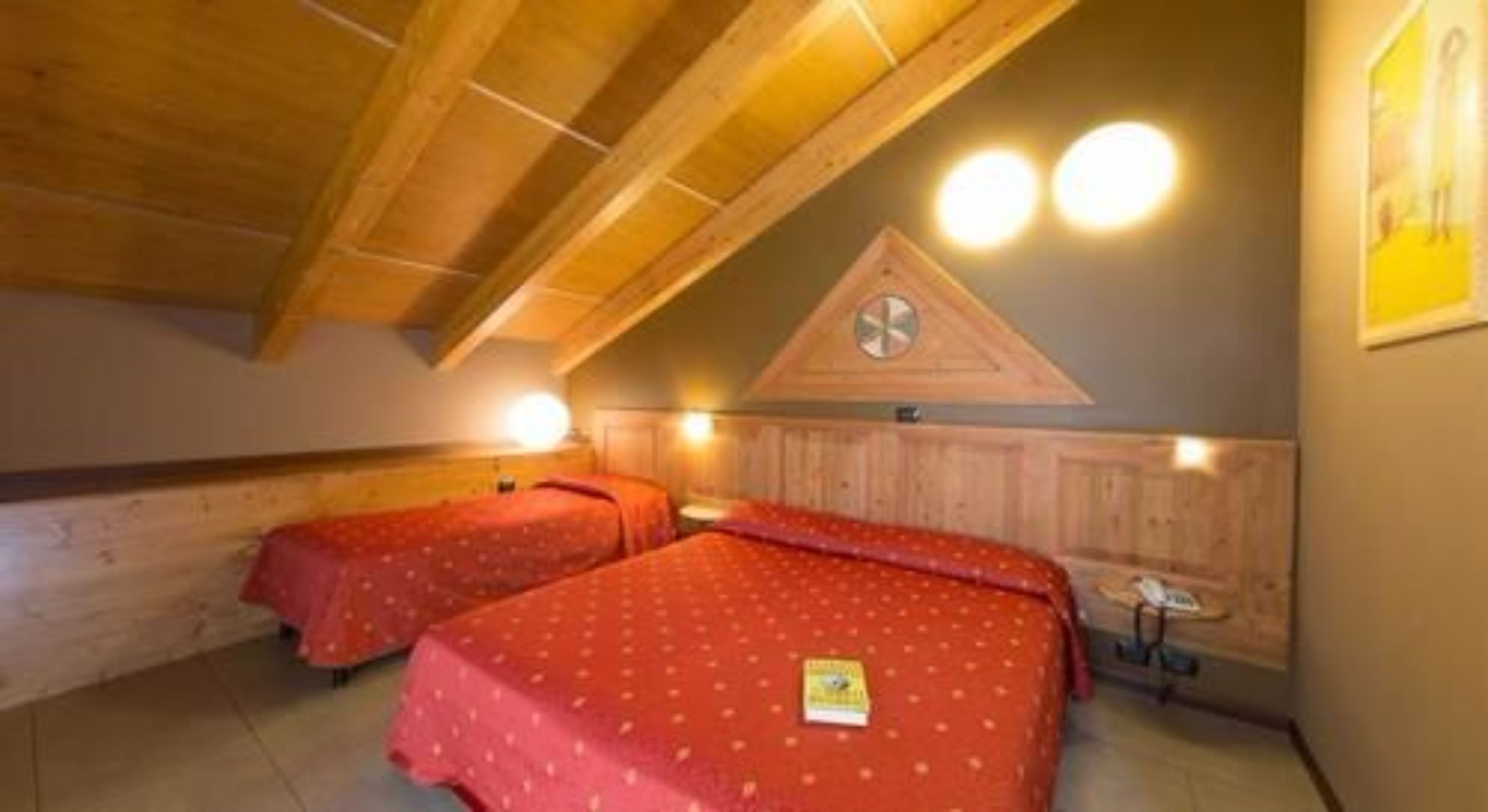 Quarto com duas camas, vigas de madeira no teto e luminária fixada na parede.