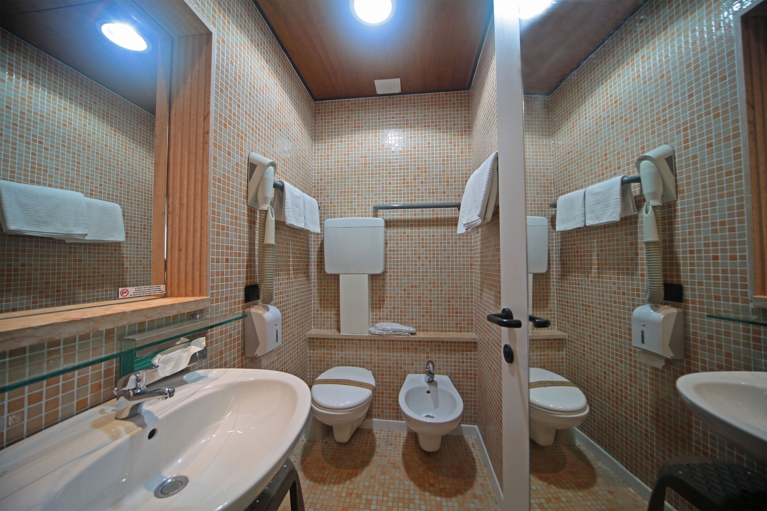 A bathroom with a large sink, two toilets, a bidet, and a glass shower enclosure.