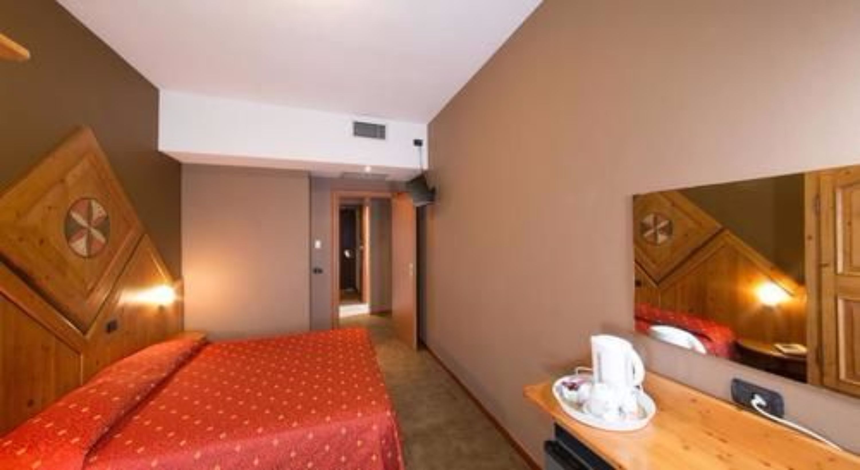 A hotel room with a bed, a desk with a telephone, and a mirror.