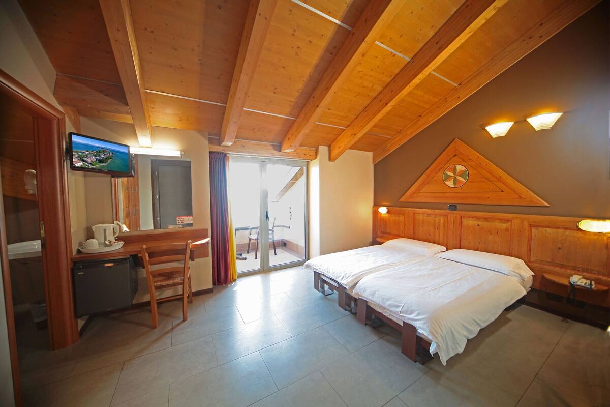 Een hotelkamer met een houten plafond, een bed, een bureau met stoel, een televisie en een badkamer met douche.