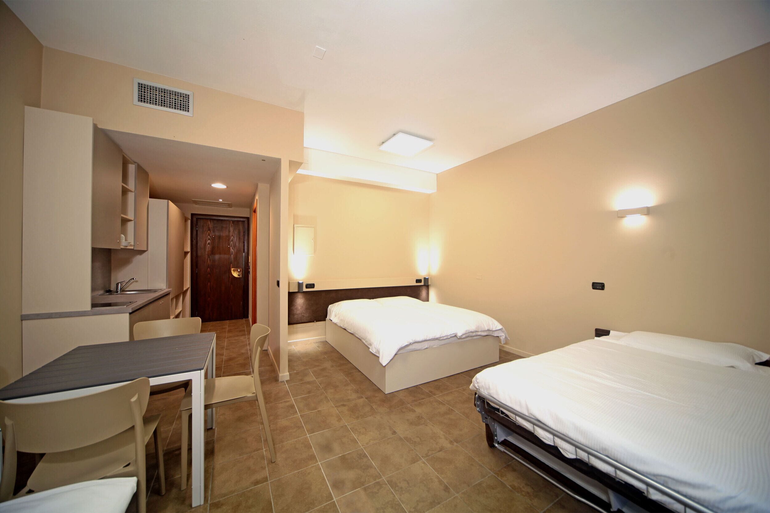 A hotel room with two beds, a kitchenette, a dining table, and a bathroom.