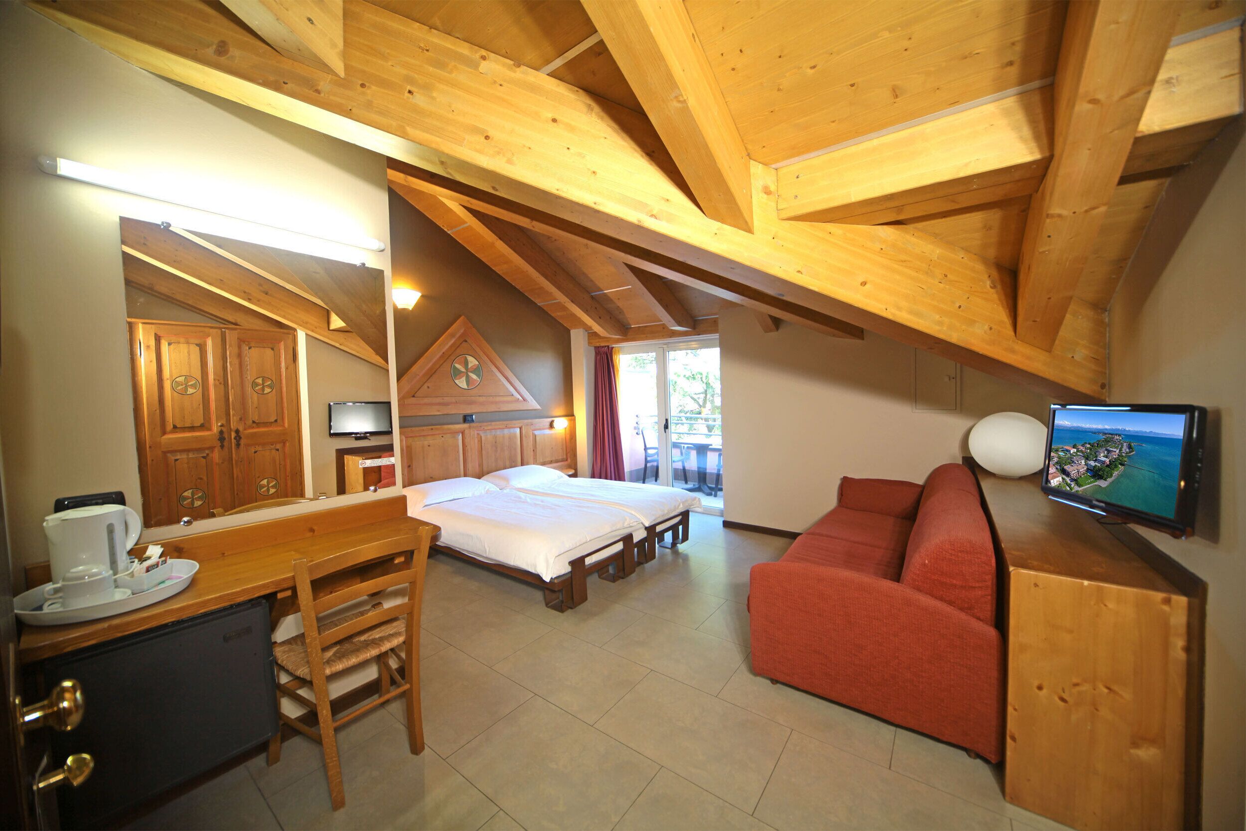 A room with a bed, a sofa, a desk with a computer, and a television.