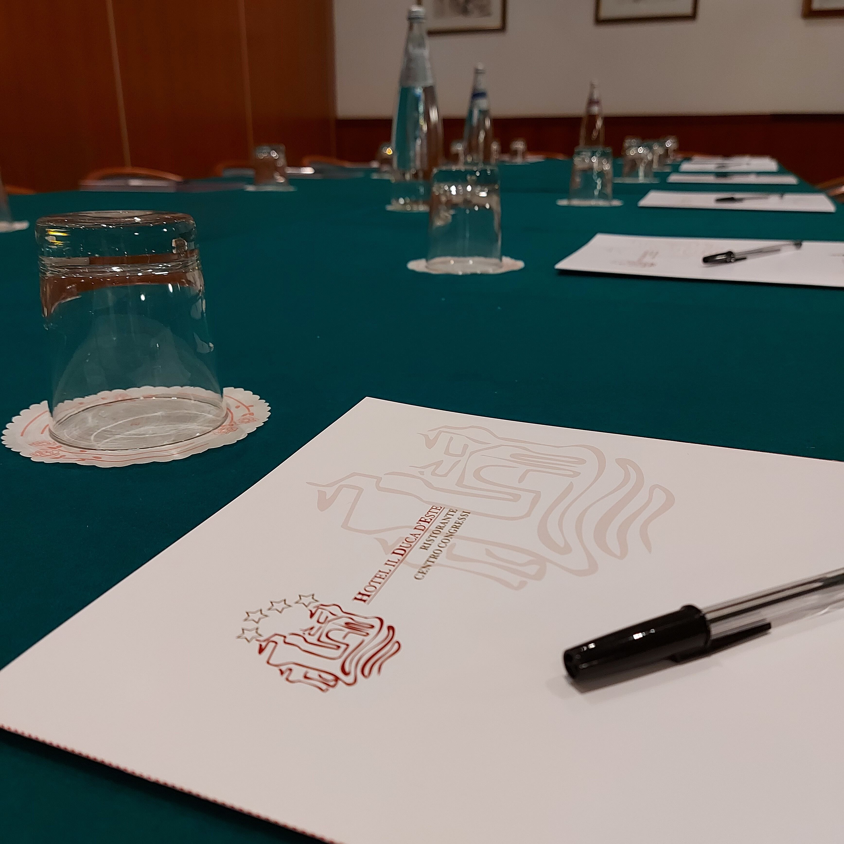 Una mesa de conferencias con un mantel individual, un vaso, un bolígrafo y un documento con un logotipo y texto.