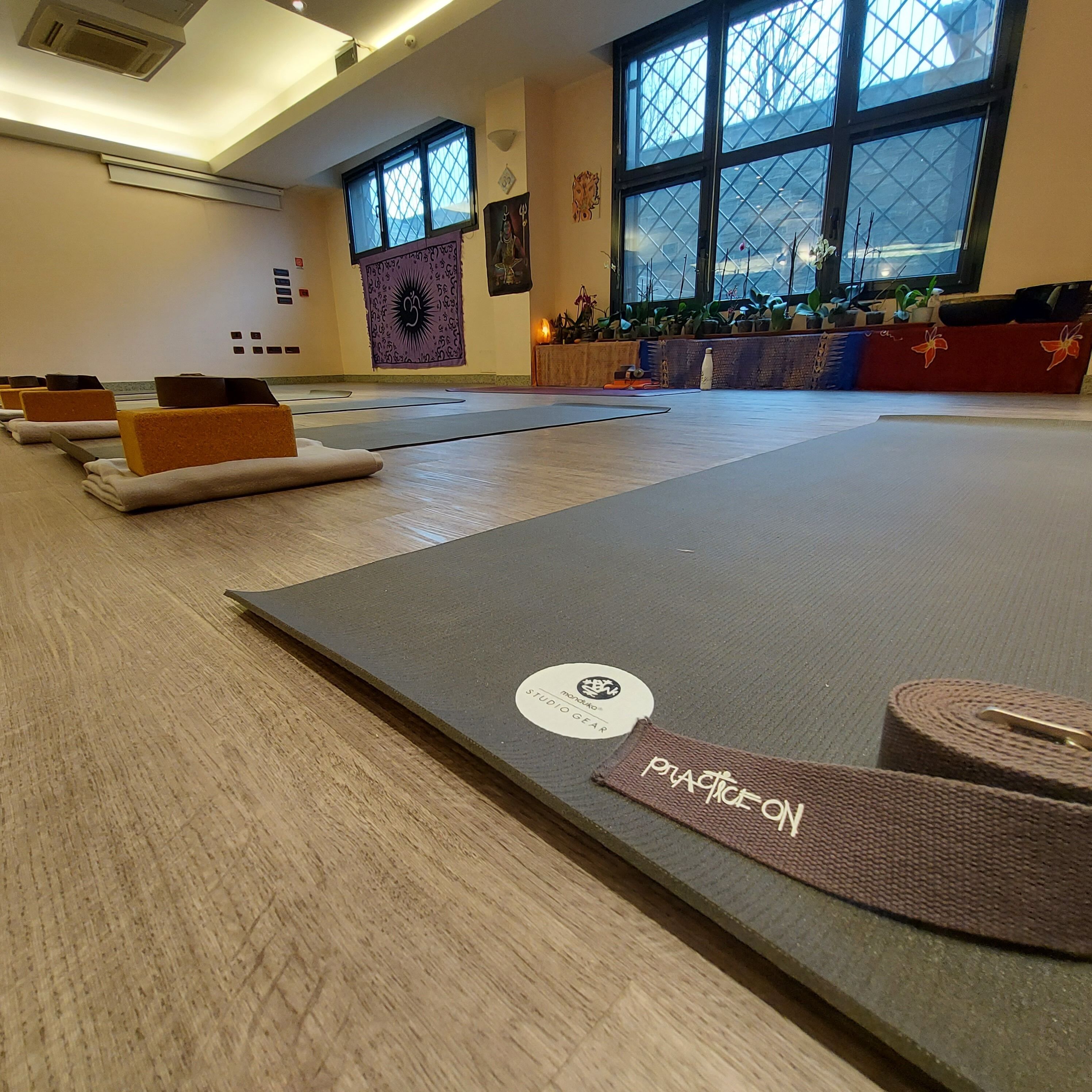 Un studio de yoga équipé de tapis, doté d’un plancher en bois, d’une grande fenêtre et d’un mur orné d’une tapisserie.