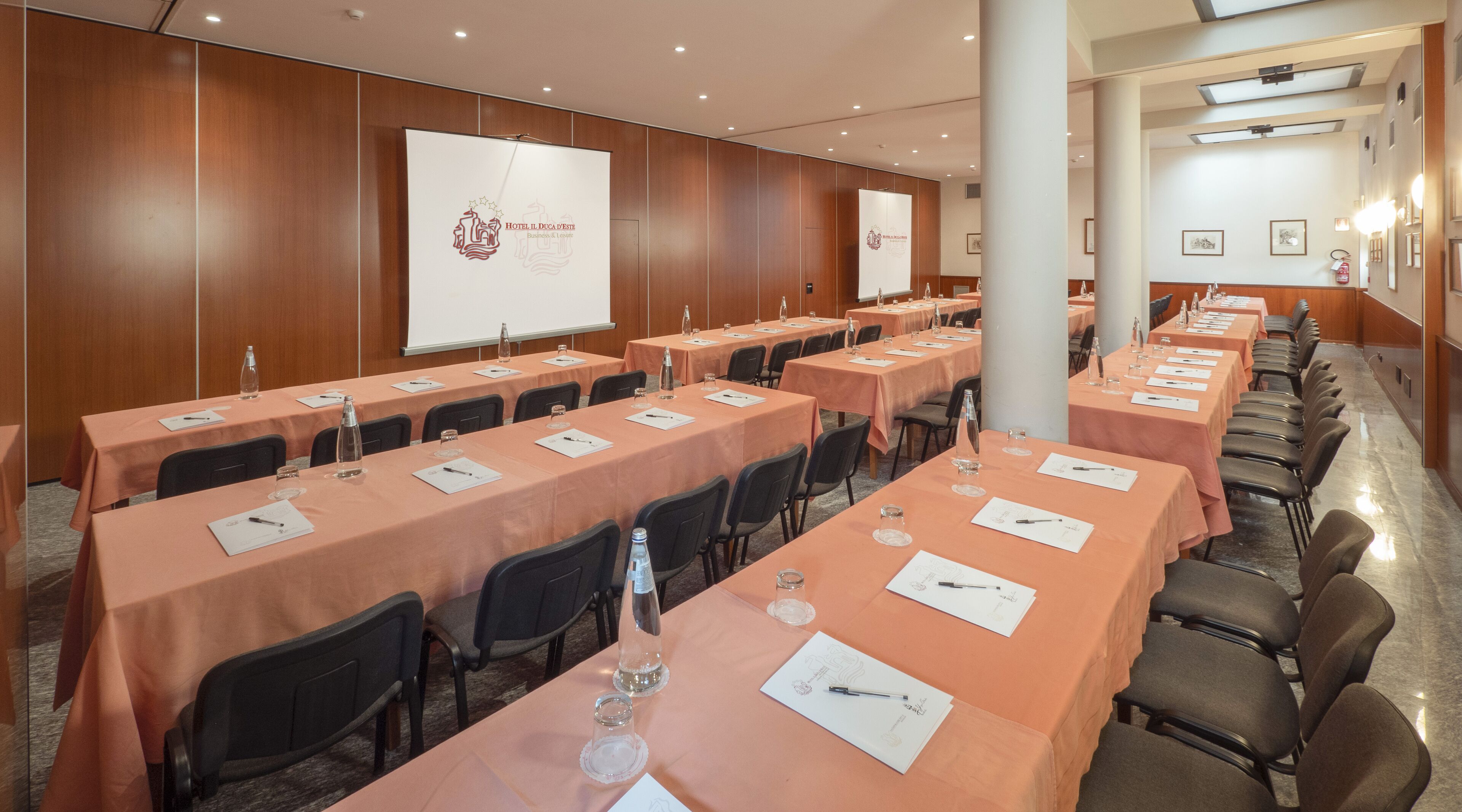 Un salón de conferencias con varias mesas, cada una con tarjetas de identificación, bolígrafos y botellas de agua.