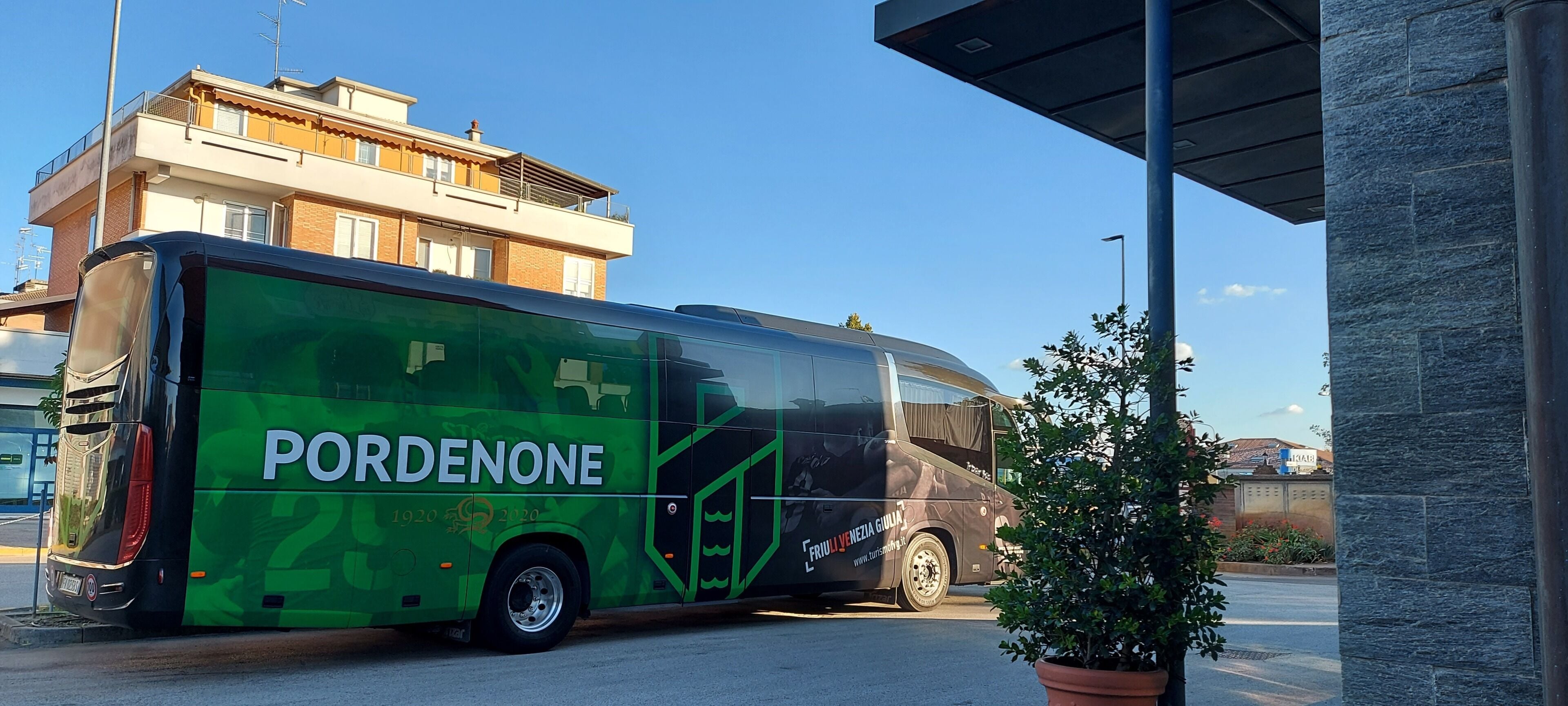 Un autobús verde con la inscripción 'PORDENONE' estacionado cerca de un edificio.
