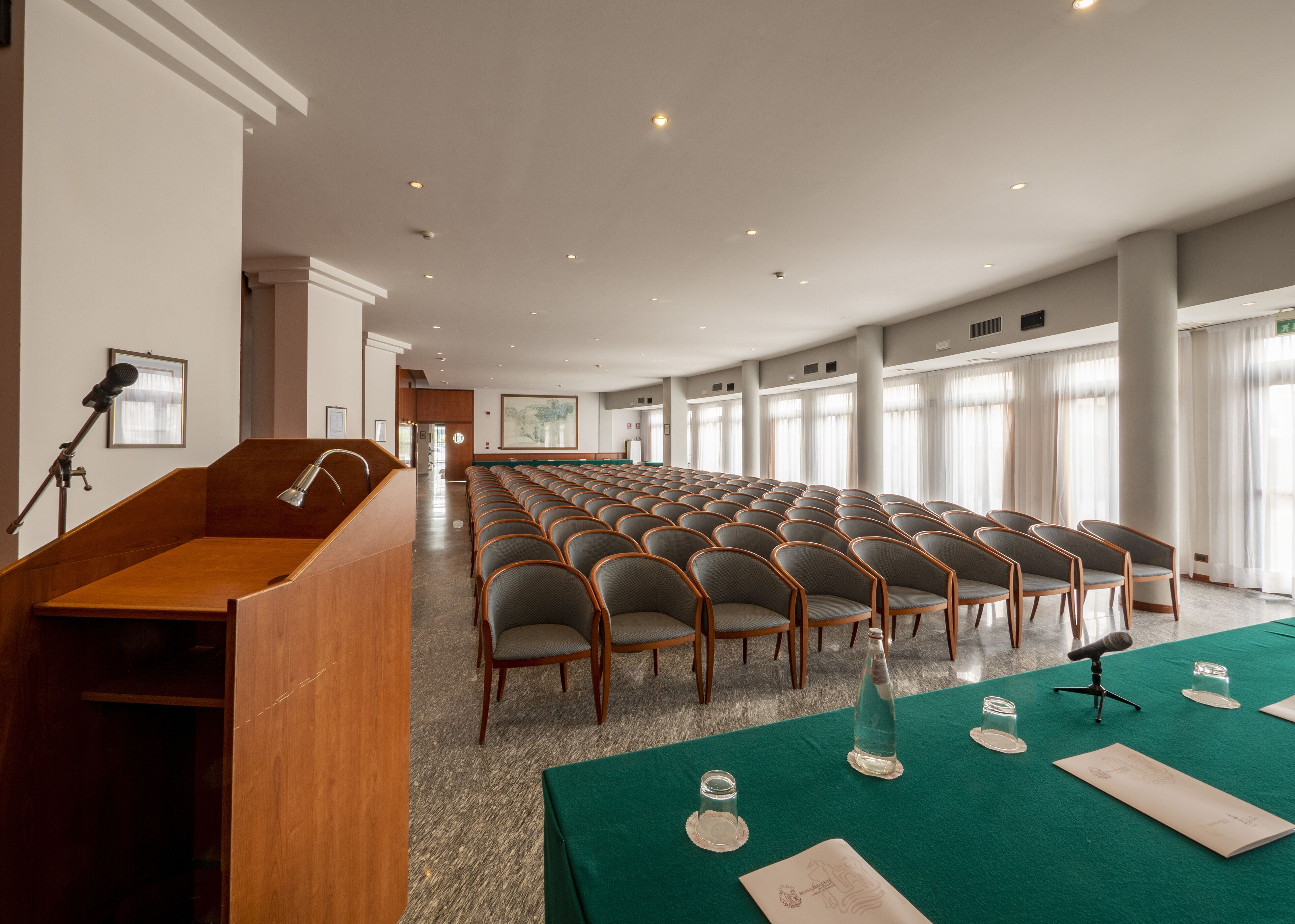 Un salón de conferencias con filas de sillas, un atril y una mesa con botellas de agua y vasos.