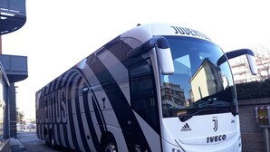 Un autobus blanc orné de bandes noires et du logo de la Juventus, garé dans une rue.