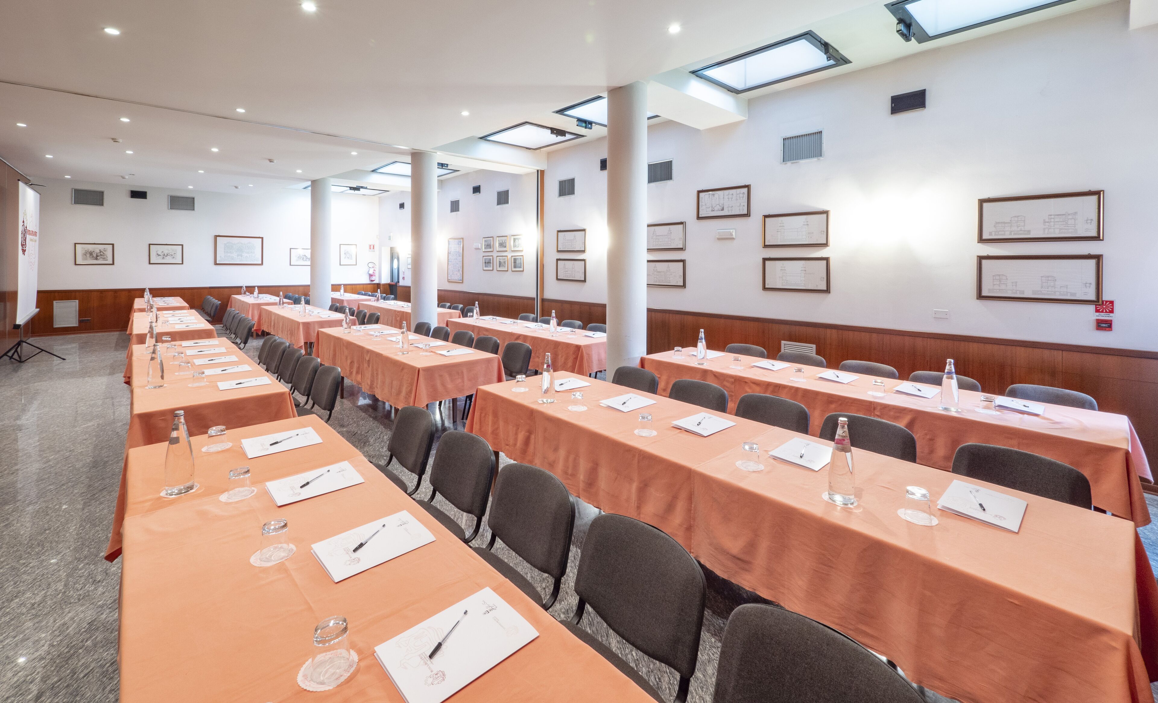 Un salón de conferencias con largas mesas, sillas y diplomas enmarcados en las paredes.