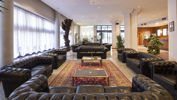 Un hall d’entrée spacieux, doté de canapés en cuir, d’une table basse centrale et d’une grande fenêtre agrémentée de rideaux.