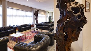 Un hall d’hôtel moderne avec des canapés en cuir, une table basse en verre et une grande sculpture en bois.