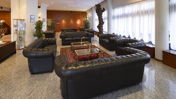 Un vestíbulo amplio con varios sofás de cuero negro dispuestos alrededor de una mesa de centro, una recepción y una gran escultura de madera.