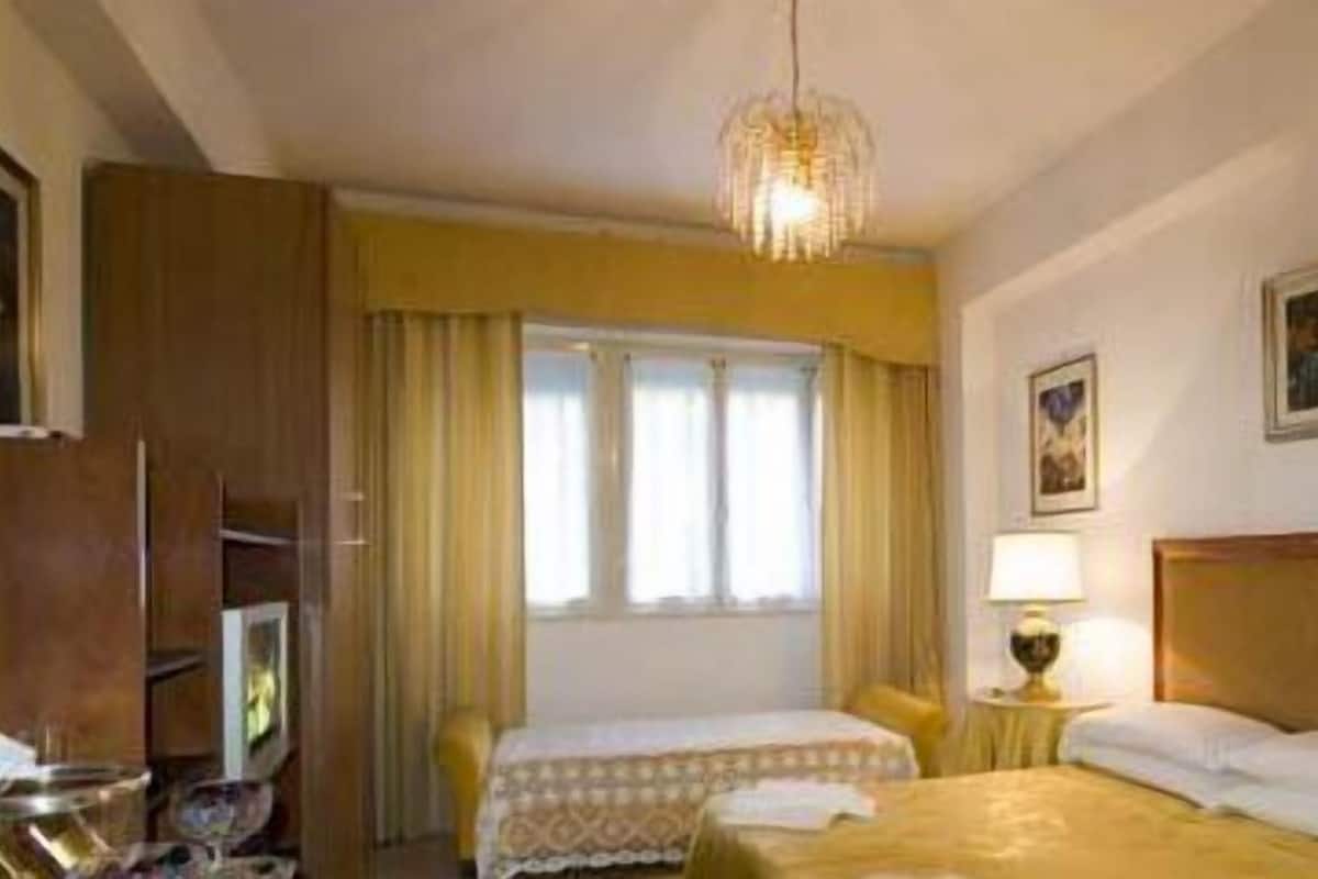 A hotel room with a bed, a chair, a desk with a lamp, and a window with curtains.