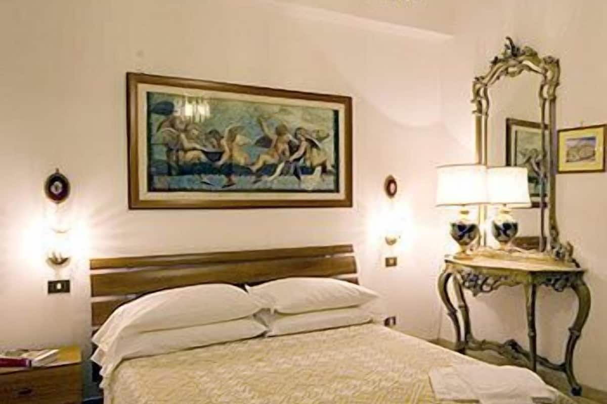 A hotel room with a bed, a painting on the wall, a chandelier, and a mirror.
