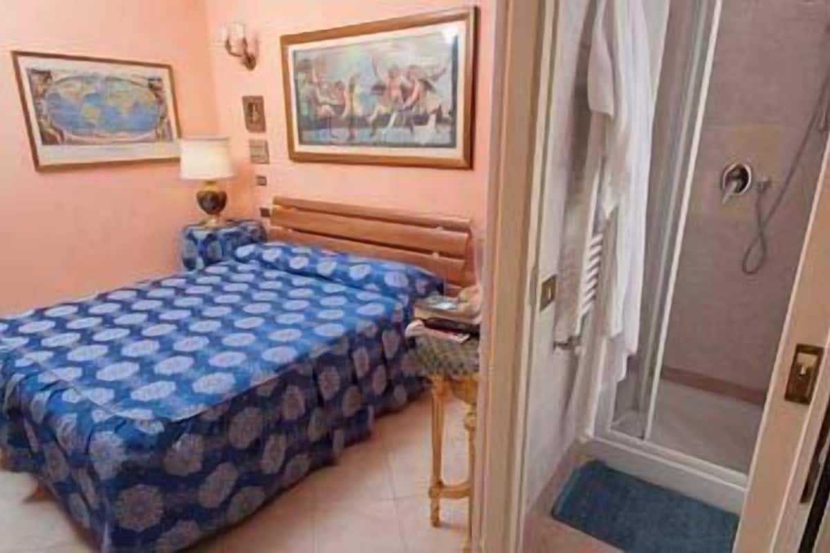 A bedroom with a bed, a nightstand, a lamp, and a door leading to a bathroom.