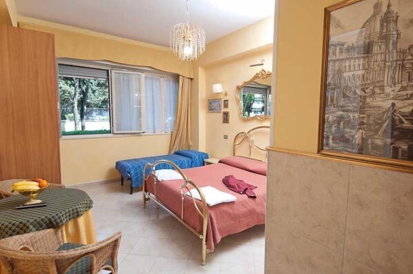 Una habitación con dos camas, una mesa de comedor con fruta, un candelabro y un cuadro en la pared.