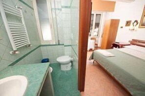 Una habitación pequeña y funcional con una cama individual, un inodoro y un lavamanos.