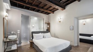 Ein modernes Schlafzimmer mit einem großen Bett, einem Nachttisch mit Lampe, einer eingebauten Bank und einem Duschbereich.