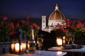 A dining table with candles and flowers, a view of a building with a dome and tower, and a night sky. - Hotel Cardinal Of Florence (Florence)
