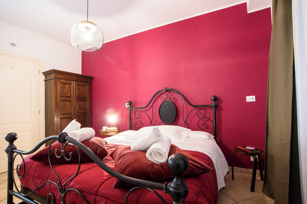 A bed with a red bedspread, a wooden wardrobe, and a small bedside table with a lamp.