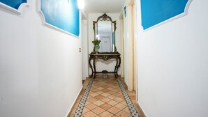 Un pasillo con suelo de baldosas, una consola con un florero y un espejo en la pared.