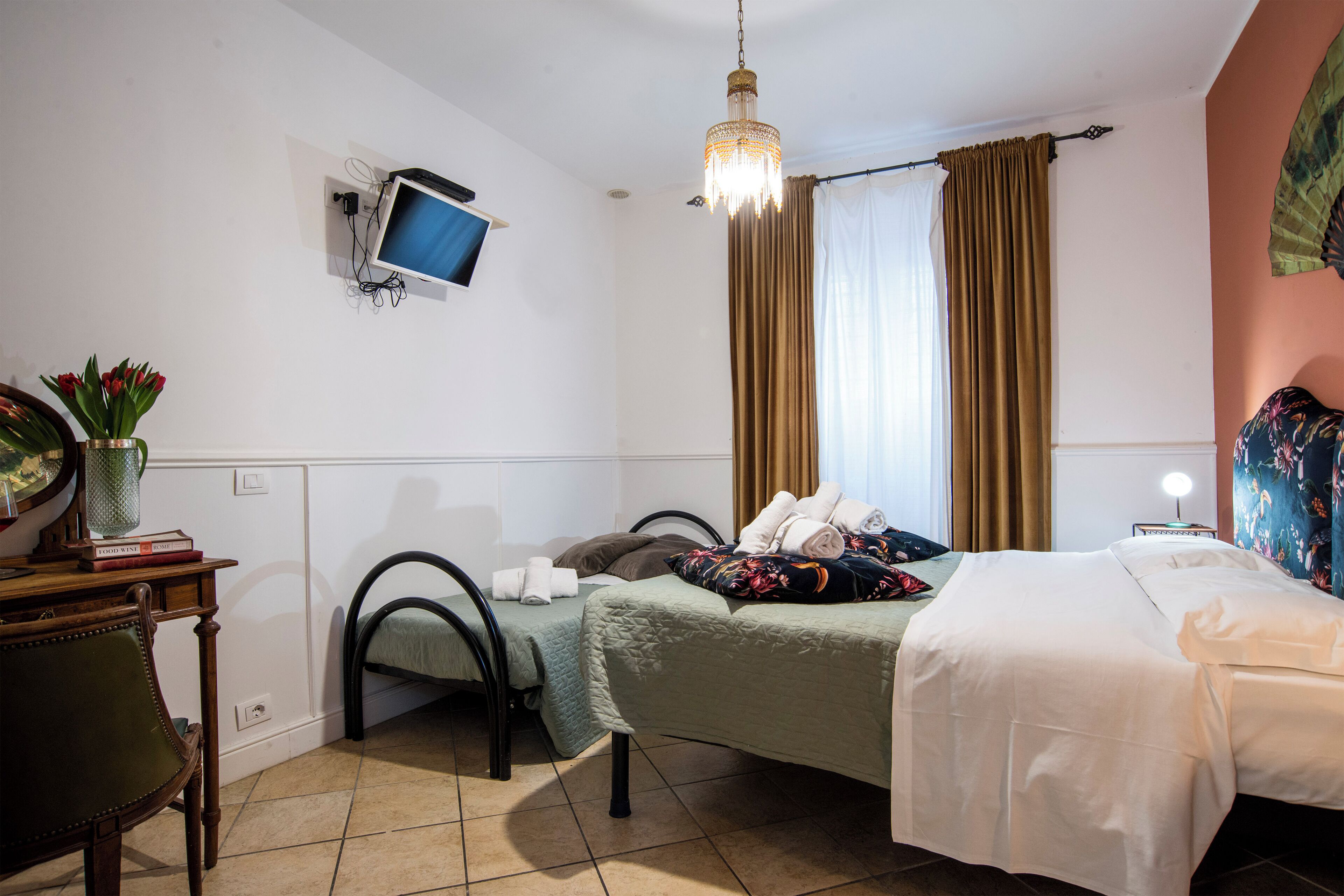 A hotel room with two beds, a desk, a chair, a television, and a chandelier.