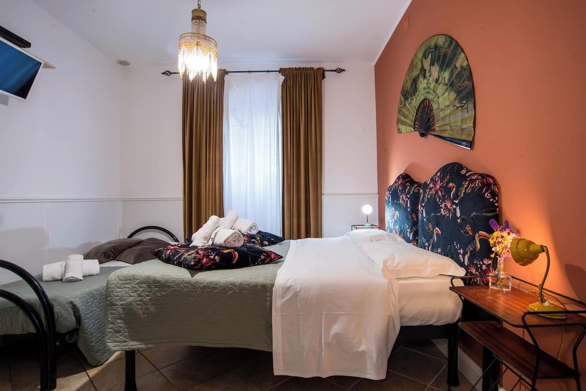 A hotel room with two beds, a desk, a chair, a lamp, and a decorative fan.