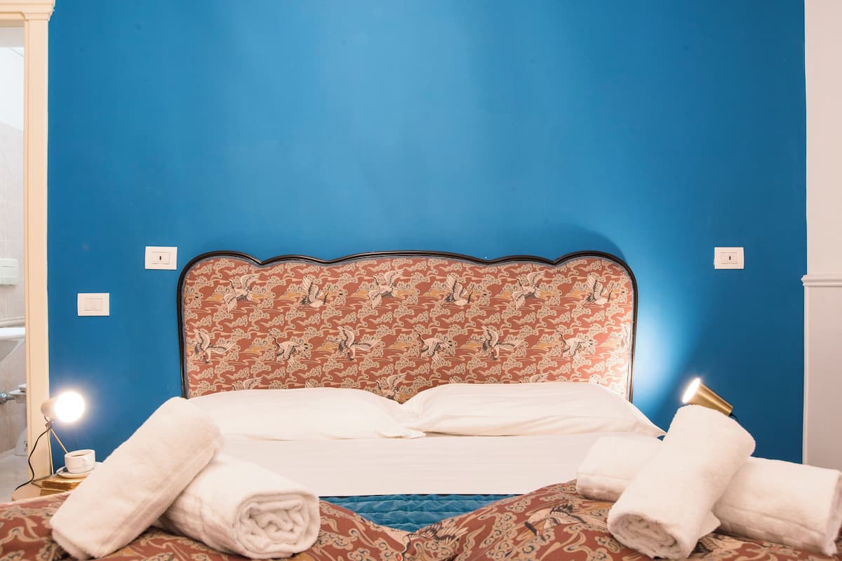 A bed with a floral headboard, white linens, and rolled towels on the bed.