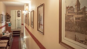 Un pasillo de hotel con cuadros enmarcados en las paredes, una escalera y un área de comedor con mesas y sillas.
