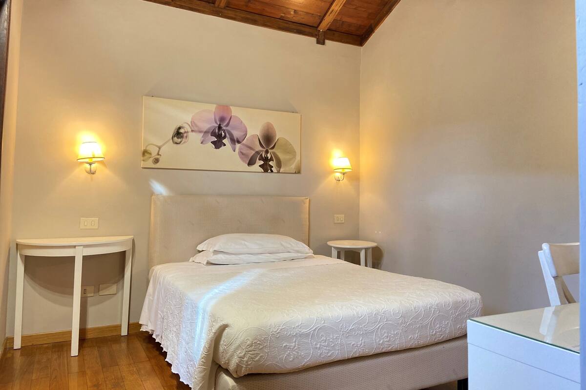 A bedroom with a bed, two bedside tables, a nightstand, a painting, and a wooden ceiling.