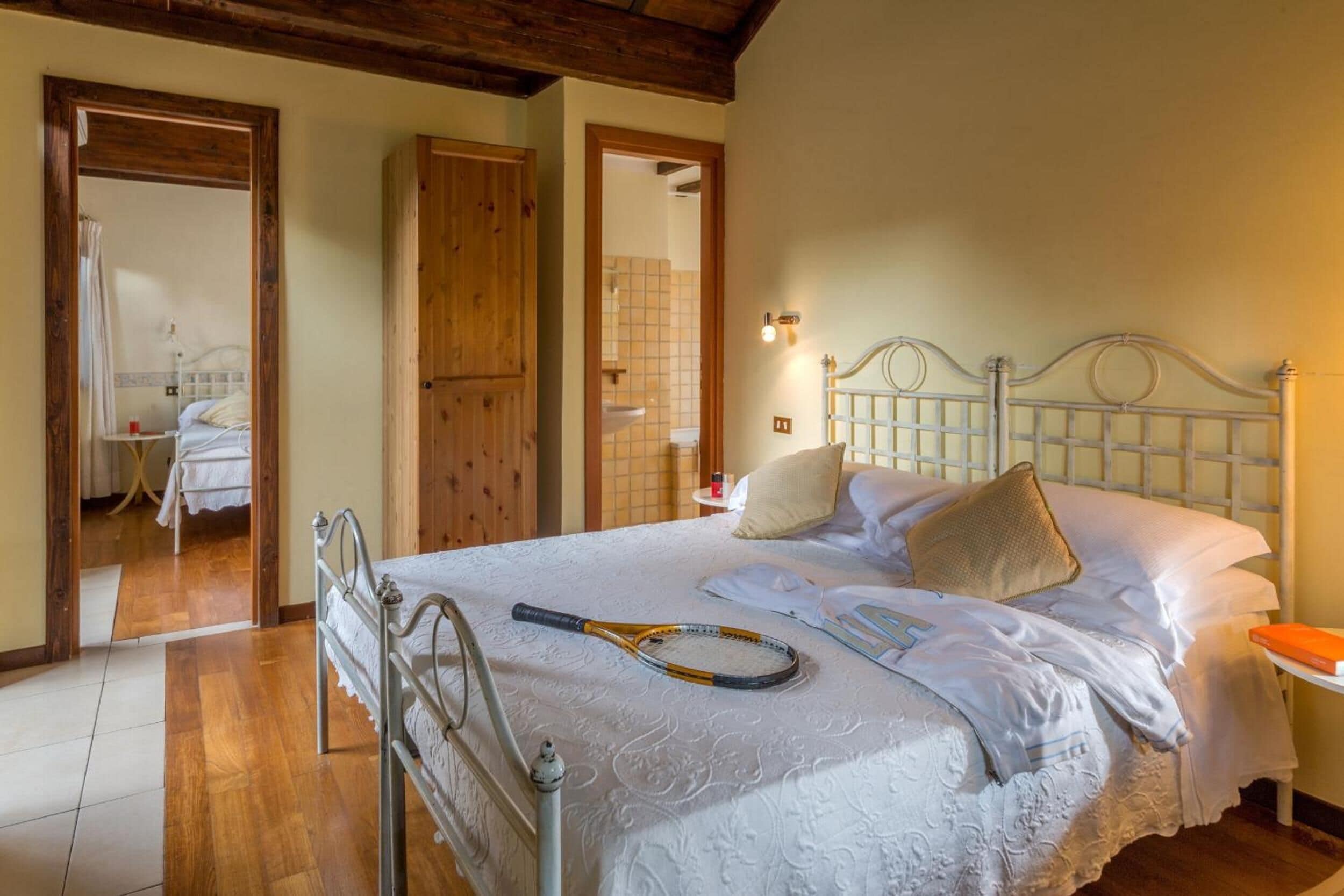 A bedroom with a bed, a wooden wardrobe, and a bathroom visible through an open door.