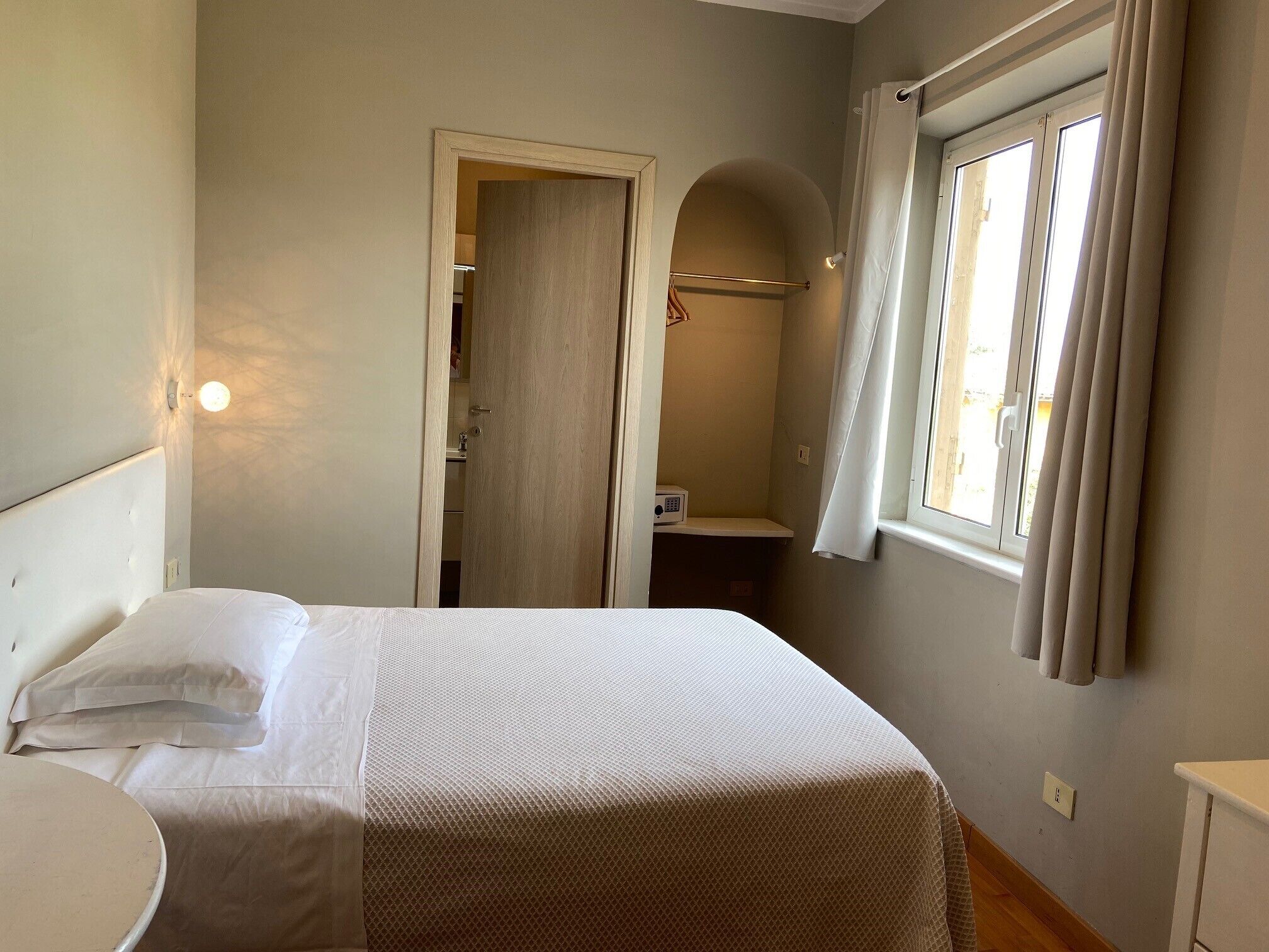 A bedroom with a bed, bedside table, and a window with curtains.