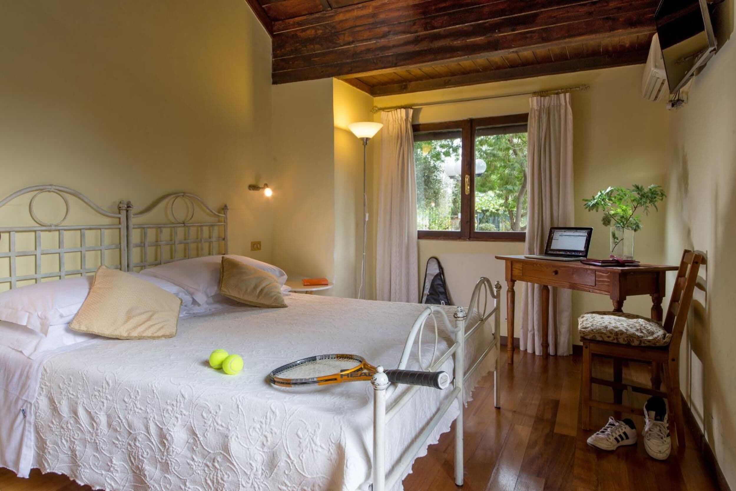 A bedroom with a bed, a desk with a laptop, a chair, tennis balls, and a tennis racket.