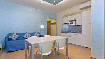 Une cuisine moderne avec des meubles blancs et un four à micro-ondes, un coin repas avec une table et des chaises, et un canapé bleu agrémenté de coussins à motifs.