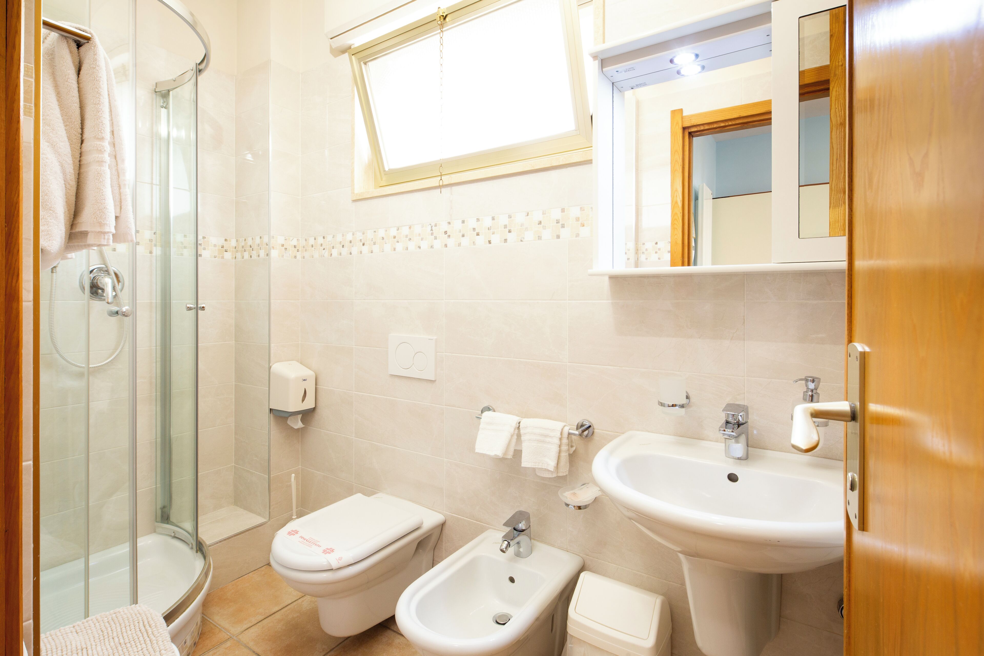 Un baño con cabina de ducha de vidrio, un bidé, un inodoro, un lavamanos y un espejo sobre el lavamanos.