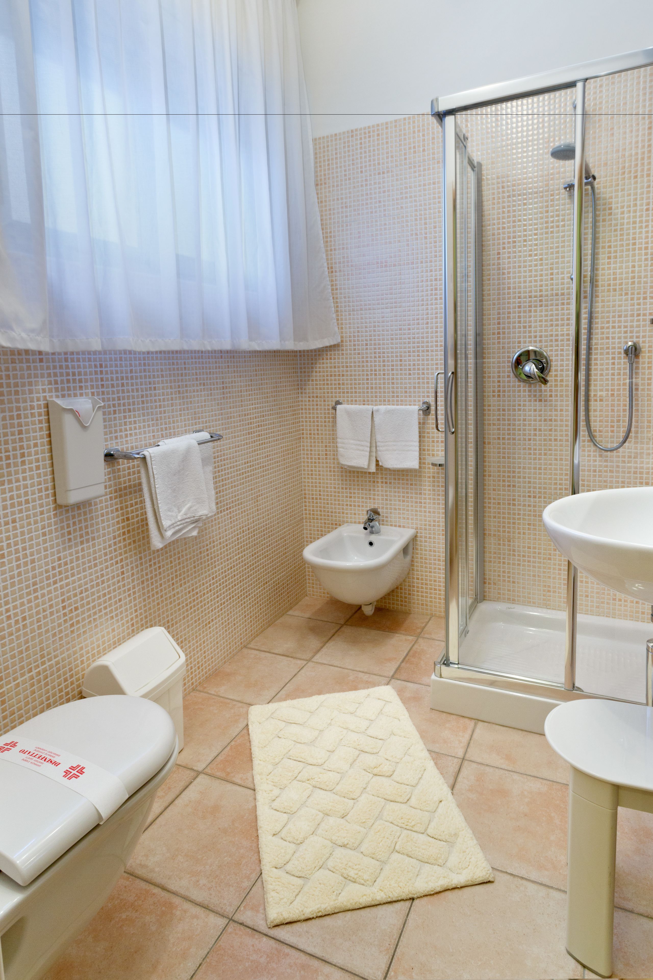 A bathroom with a shower, bidet, sink, toilet, and a towel rack.