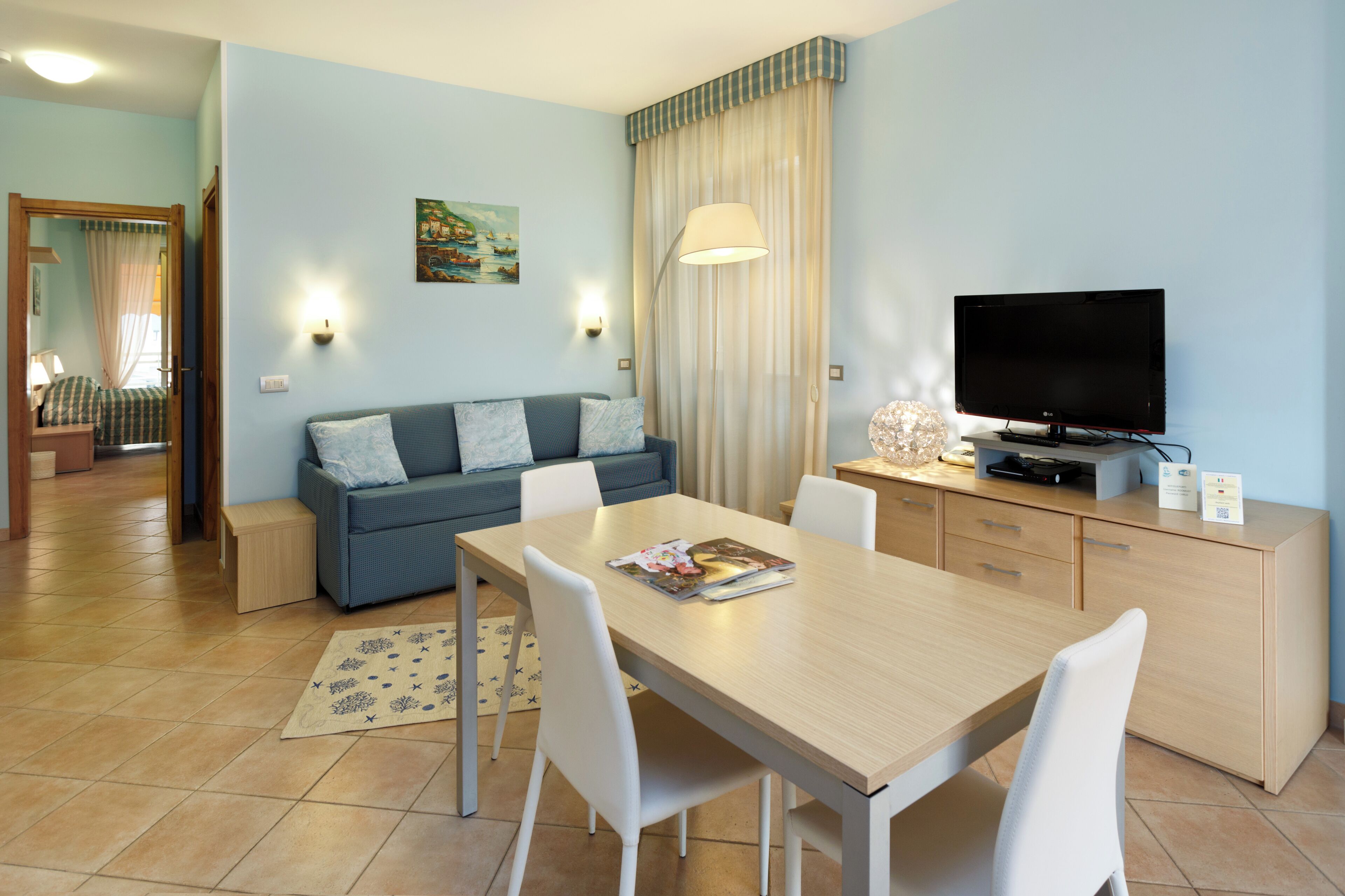 A modern living room with a sofa, dining table, TV, and a painting on the wall.