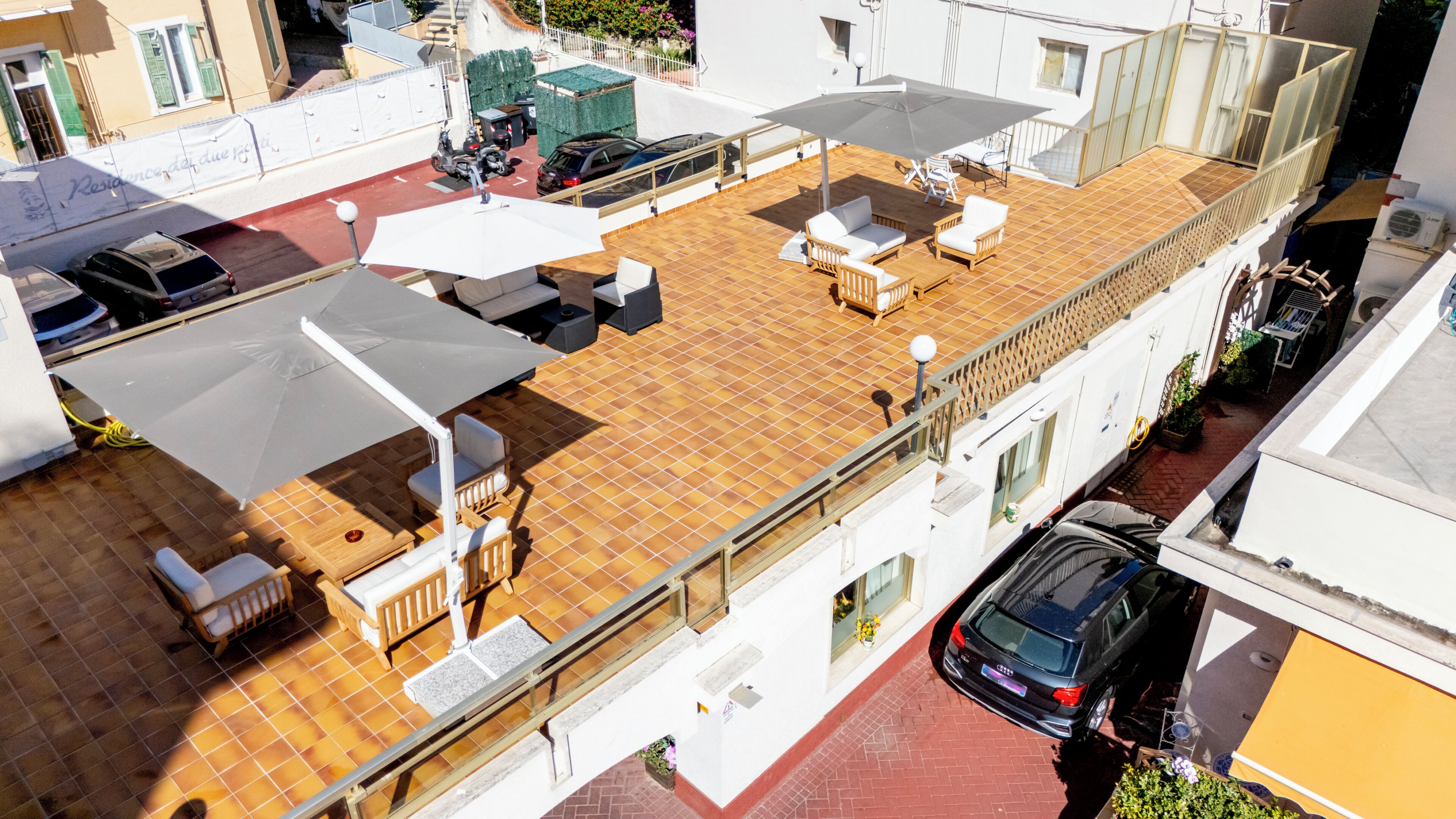 Una terraza en la azotea con mobiliario exterior, un coche y un edificio de fachada blanca.