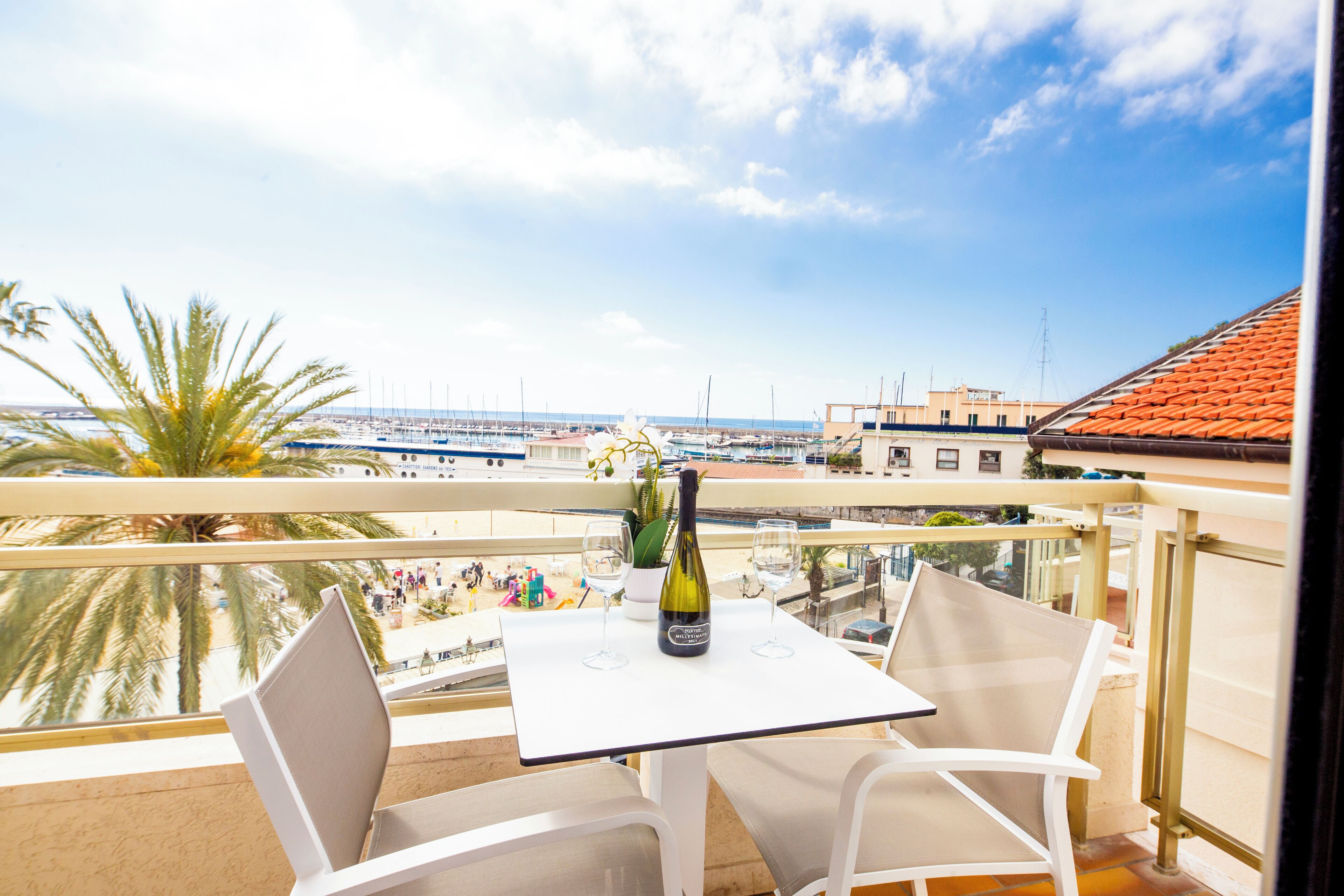 Un balcon avec une table, deux chaises, une bouteille de vin et une vue sur le port de plaisance.