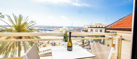 A balcony with a table, two chairs, a bottle of wine, and a view of the marina.